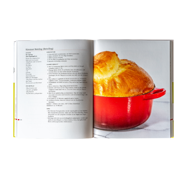Open cookbook with a recipe on the left and a red pot with baked bread on the right.