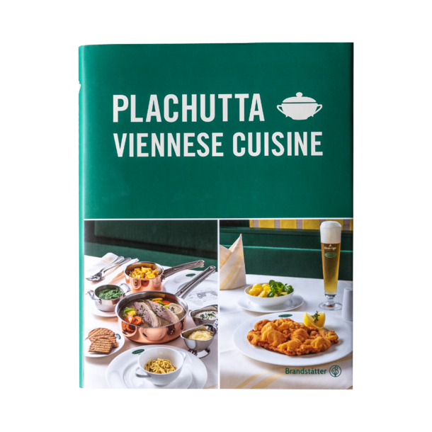 Paniertes Schnitzel mit einer Zitronenspalte auf einem weißen Teller, mit einer Gabel und einer Beilage im Hintergrund.