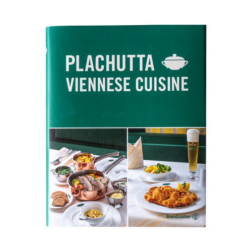 Paniertes Schnitzel mit einer Zitronenspalte auf einem weißen Teller, mit einer Gabel und einer Beilage im Hintergrund.