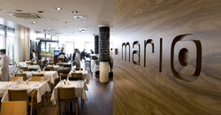 Modernes Restaurantinterieur mit hölzernen Akzenten, weißen Tischtüchern und einem Mario-Schild an der Wand.